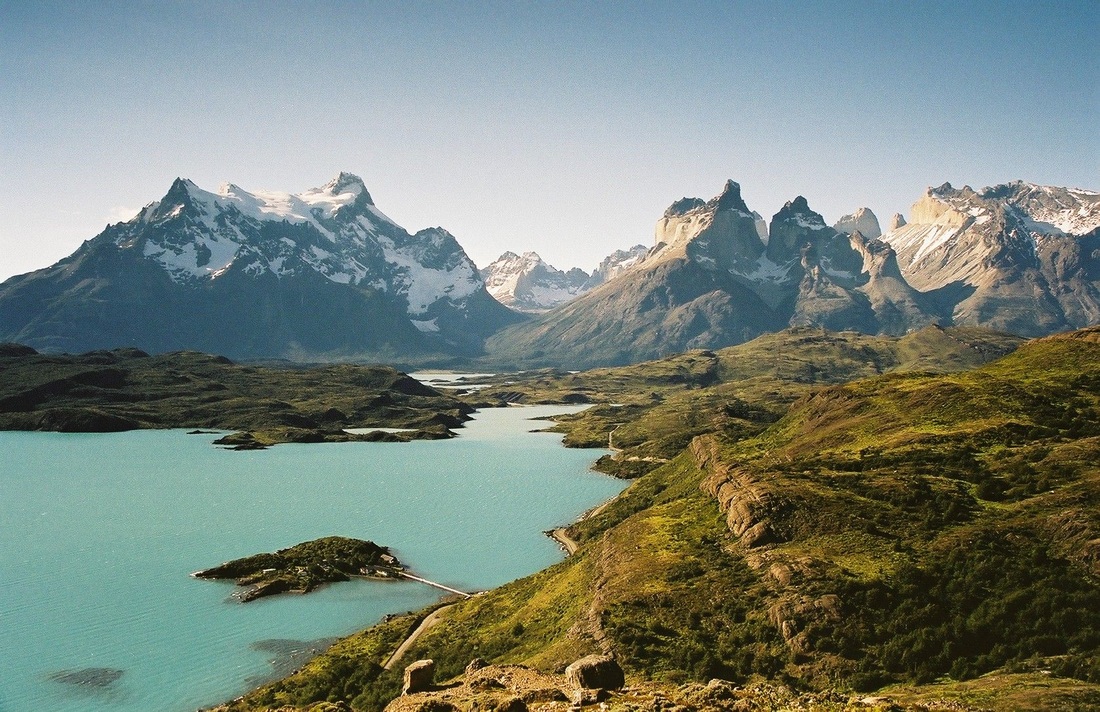 Lac turquoise entouré de sommets andins enneigés et de collines verdoyantes sous un ciel dégagé